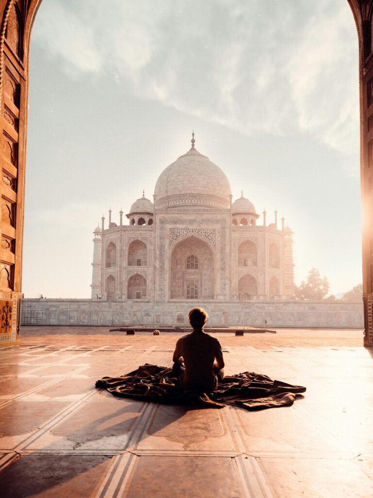 A person meditates at sunrise facing the iconic Taj Mahal, capturing serenity and majesty.